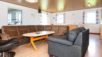 En stue med en krogsofa, et rundt sofabord og et spiseområde med et køkken i baggrunden.