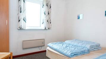 Et soveværelse med en enkeltseng, et vindue med gardiner, en radiator og et lille bord.