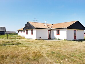 A single-story building with a red door and windows, surrounded by a grassy field.