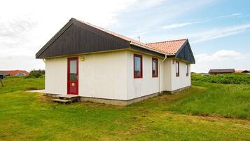 A single-story building with a red door and windows, surrounded by grass and a clear sky.