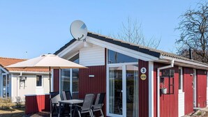 A red building with a satellite dish, a covered patio with a table and chairs, and a glass door entrance.