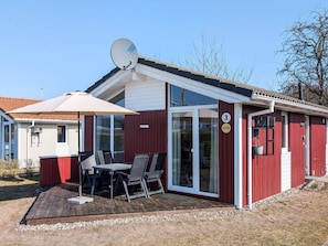 A red building with a satellite dish, a covered patio with a table and chairs, and a glass door entrance.