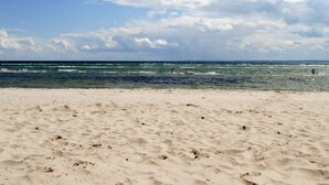 A beach with sand and waves, under a partly cloudy sky.