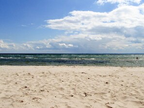 A beach with sand and waves, under a partly cloudy sky.