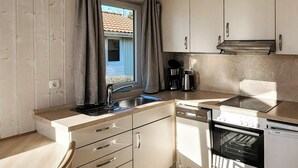A compact kitchen with a sink, dishwasher, and stove, wooden cabinets, and a window with curtains.
