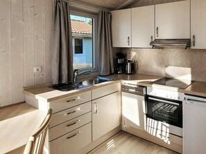 A compact kitchen with a sink, dishwasher, and stove, wooden cabinets, and a window with curtains.