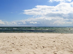 Ein sandiger Strand mit Wellen und einem teilweise bewölkten Himmel.