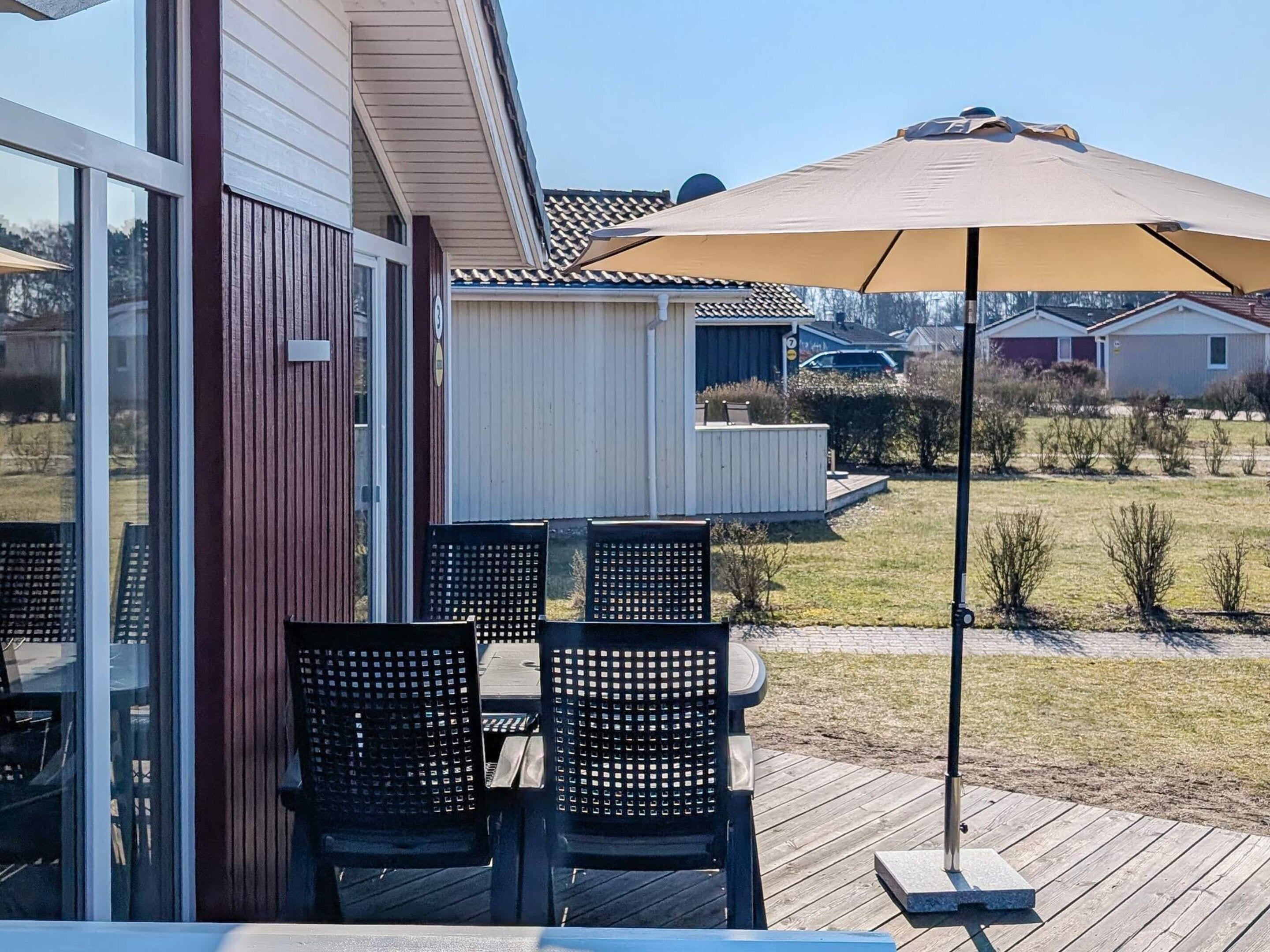 An outdoor patio with a table and chairs, a large umbrella, and a view of a residential area.