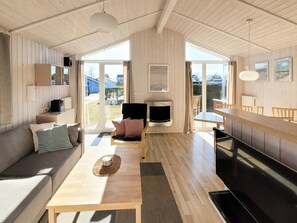 A modern interior with a wooden floor, a sofa, a dining table, a fireplace, and large windows.