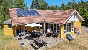 Ein gelbes Gebäude mit rotem Ziegeldach, Solaranlagen und Außenplätzen.