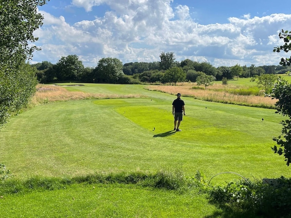 A golf course with a person standing on the green, surrounded by trees and open grassy areas.