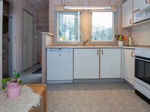 A compact kitchen with a dishwasher, a stove, and a window with a view of trees.