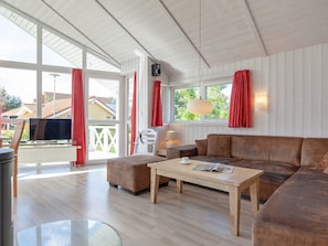 A spacious living room with a wooden floor, a brown sofa, a wooden coffee table, and a television on a stand.