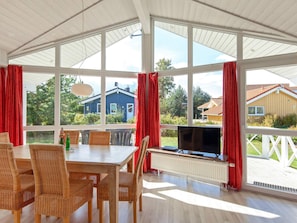 A room with a large window, a dining table, chairs, a television, and a radiator.