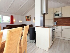 Cozinha moderna com micro-ondas, fogão e uma ilha grande. Há uma área de jantar com cadeiras de vime e uma mesa.