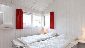 A room with two beds, a window with red curtains, a bedside table with a lamp, and a mirror on the wall. - Holiday Home in GrÃ¶mmitz (Groemitz)