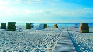 A beach with a wooden boardwalk leading to beach huts numbered 97, 99, and 64. - Holiday Home in GrÃ¶mmitz (Groemitz)