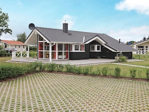 Ett modernt hus med en stor glasfasad, en inglasad veranda och en asfalterad uppfart.