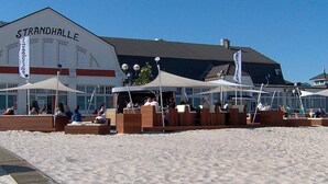 A beachside restaurant named Strandhalle with outdoor seating and umbrellas. - Holiday Home in GrÃ¶mmitz (Groemitz)