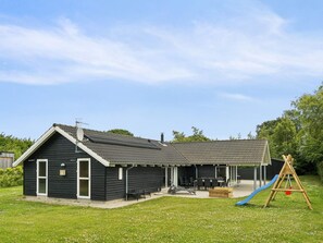 A two-story house with a covered patio, a slide, and a swing set in the backyard. - 5 Star Holiday Home in Ebeltoft (Ebeltoft)
