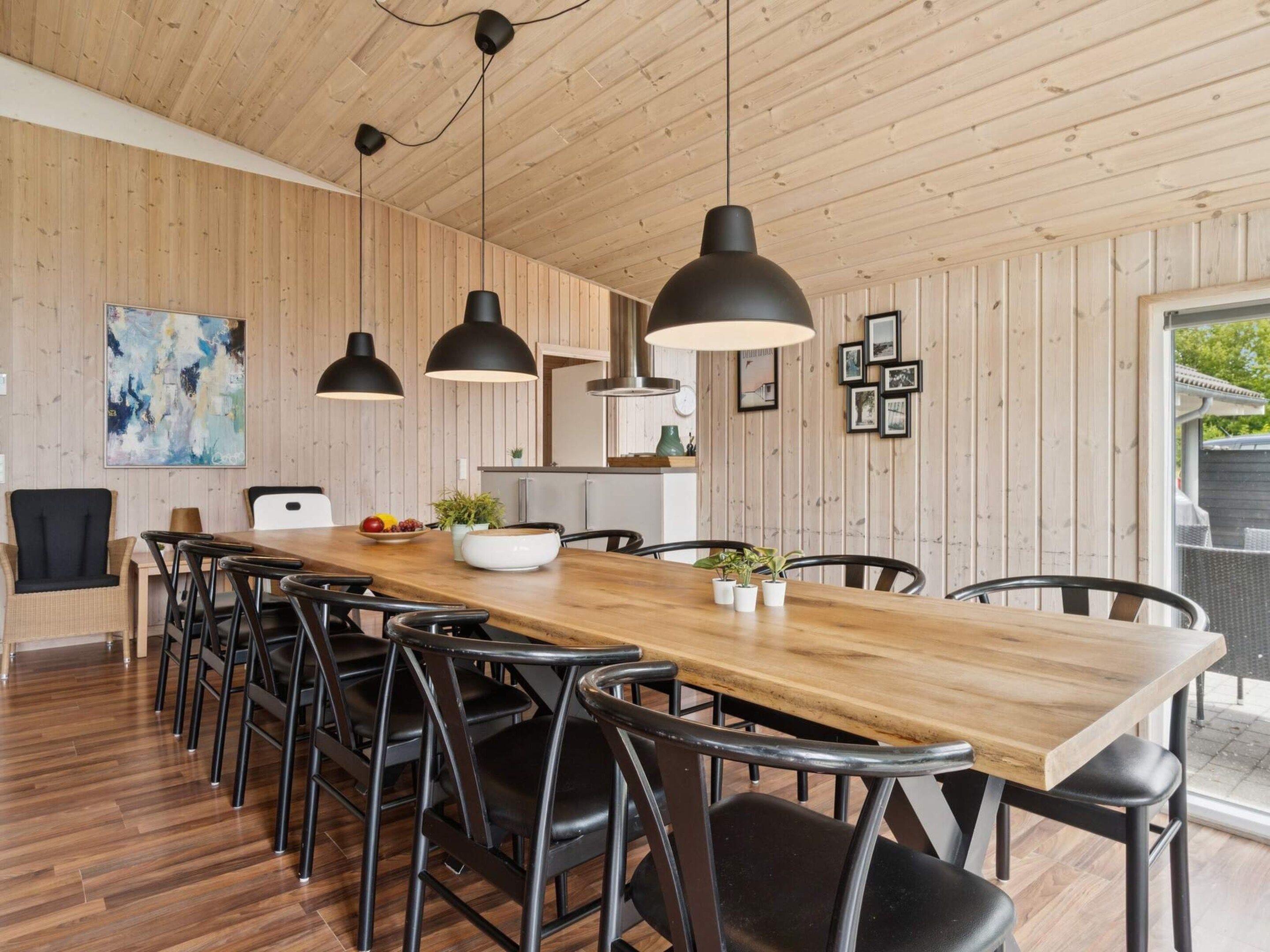 A modern dining area with a wooden table, black chairs, pendant lights, and a large abstract painting on the wall.