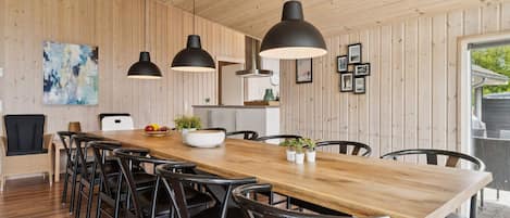 A modern dining area with a wooden table, black chairs, pendant lights, and a large abstract painting on the wall.