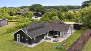 A two-story house with a covered patio and a swing set. - 5 Star Holiday Home in Ebeltoft (Ebeltoft)