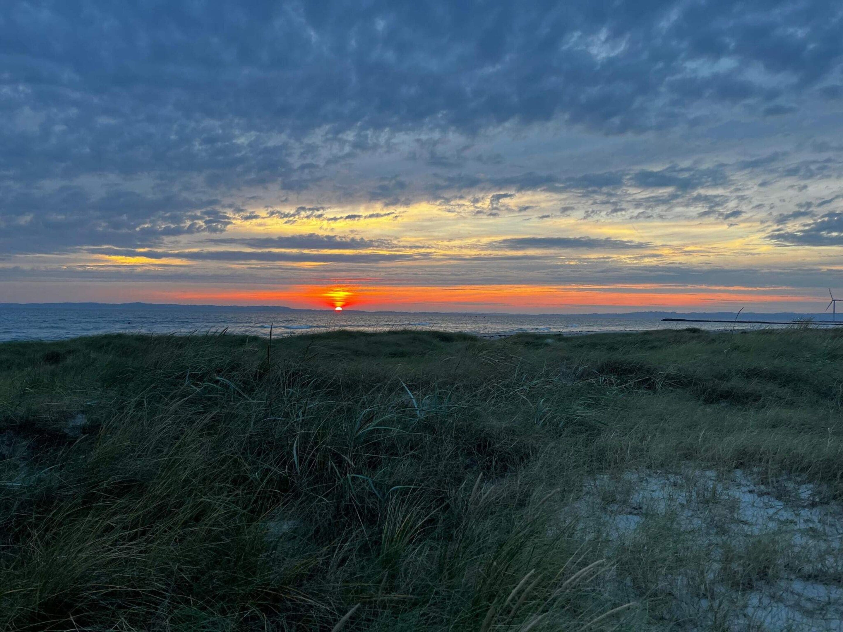 Un tramonto su una spiaggia con turbine eoliche in lontananza.
