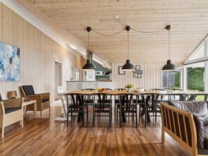 A spacious dining area with a long wooden table, black chairs, and pendant lights.