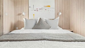 A bedroom with a bed, pillows, a blanket, a wall-mounted artwork, and two wall sconces. - Holiday Home in GrÃ¶mmitz (Groemitz)