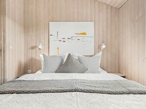 Ein Schlafzimmer mit einem Bett, Kissen, einer Decke, einem Wandbild und zwei Wandleuchten.