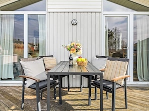 A covered patio with a table and chairs, a clock on the wall, and a view of the outside. - Holiday Home in GrÃ¶mmitz (Groemitz)
