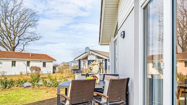 A deck with two wicker chairs and a table, overlooking a residential area with houses and a garden. - Holiday Home in GrÃ¶mmitz (Groemitz)