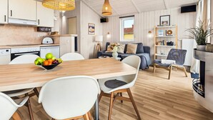 A modern kitchen with white cabinets, a wooden dining table, and a fruit bowl. - Holiday Home in GrÃ¶mmitz (Groemitz)