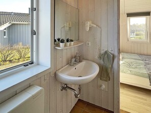 Bathroom features a sink, mirror, and potted plants on shelves, with a window offering a view of the surrounding area.