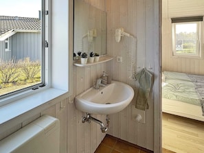 Bathroom features a sink, mirror, and potted plants on shelves, with a window offering a view of the surrounding area.