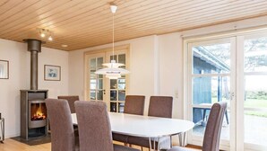 Un coin repas comprenant une table ronde, six chaises, un poêle à bois et une grande fenêtre donnant sur l’extérieur.