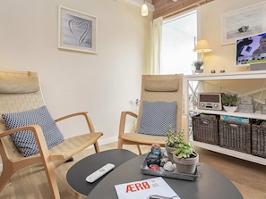 Ein Zimmer mit zwei Holzstühlen, Sitzkissen mit Muster, einem kleinen runden Tisch mit Fernbedienung, einer Zeitschrift und einer Ablage mit Dekoration.