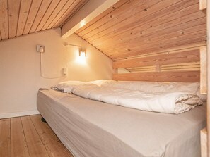 En enkelt seng i et rum med træbjælker i loftet og en vægmonteret lysarmatur.