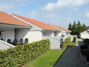 A row of white buildings with red roofs, a paved pathway, and green hedges.