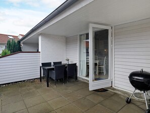 A patio with a table and chairs, a sliding glass door, and a barbecue grill.