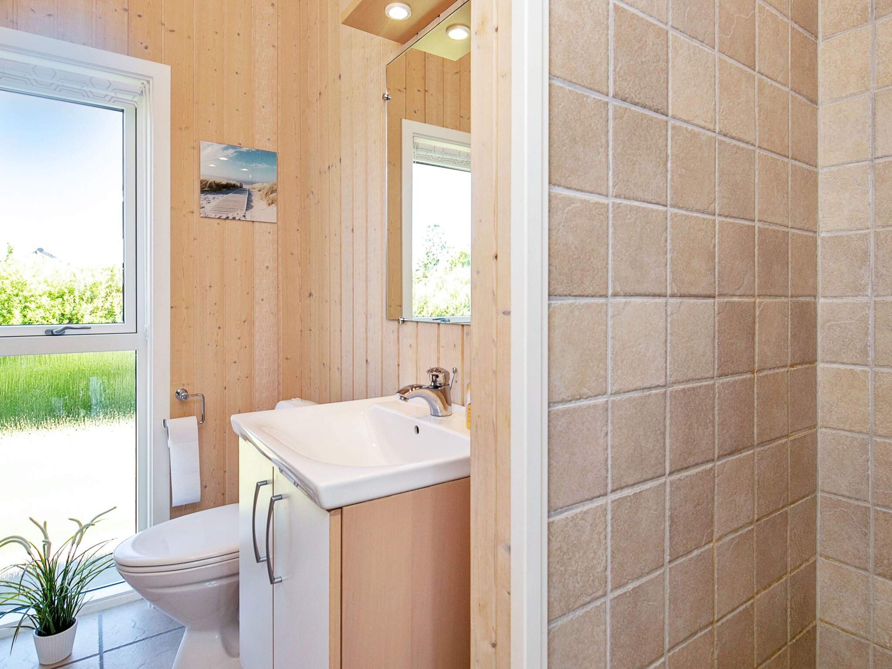 Een badkamer met toilet, wastafel en spiegel, houten wanden en een raam.