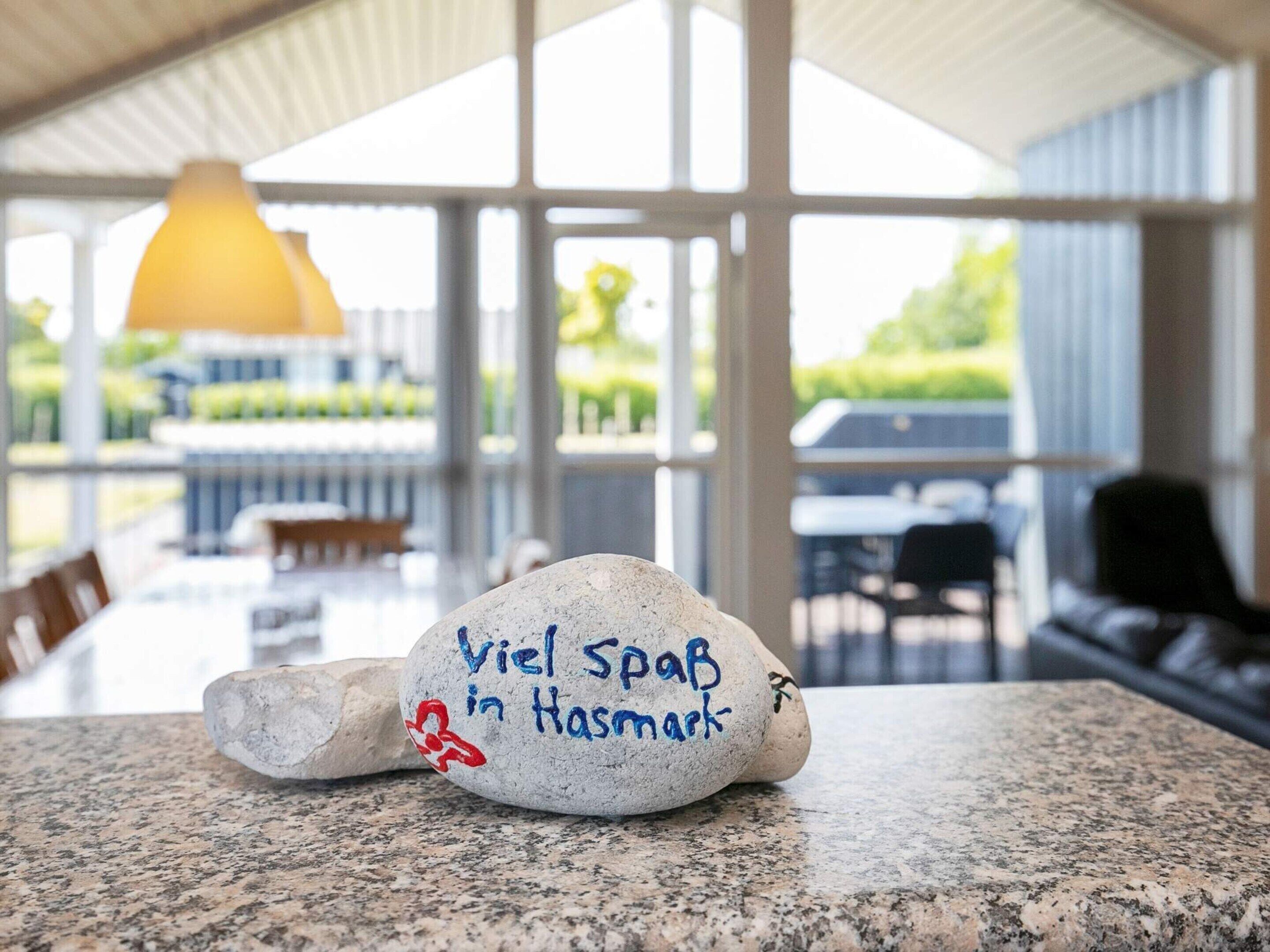 A stone with text on a countertop, a dining area with tables and chairs, and a view of greenery through large windows.