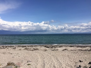 A beach with a clear sky, calm sea, and a sandy shore with some rocks.
