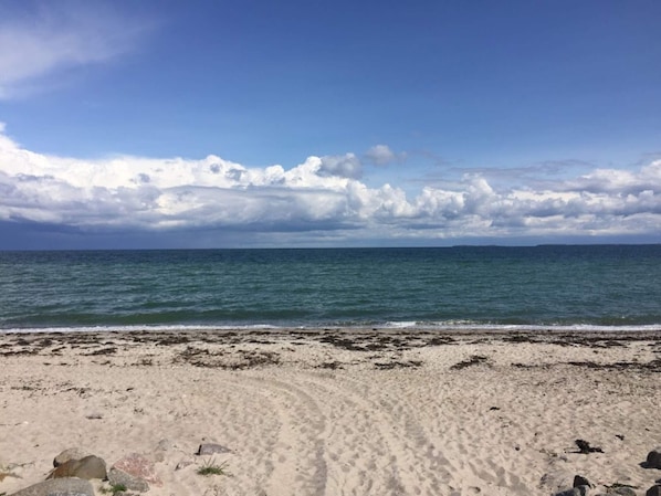 A beach with a clear sky, calm sea, and a sandy shore with some rocks.