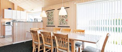 A modern kitchen with wooden cabinets, a dining table with chairs, and pendant lights.