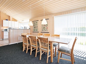 A modern kitchen with wooden cabinets, a dining table with chairs, and pendant lights.