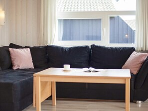 A modern living room with a dark-colored sofa, a small wooden table, and a window with curtains. - Holiday Home in GrÃ¶mmitz (Groemitz)