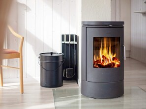 A modern room with a wood-burning stove, a metal bucket, and a wooden chair.