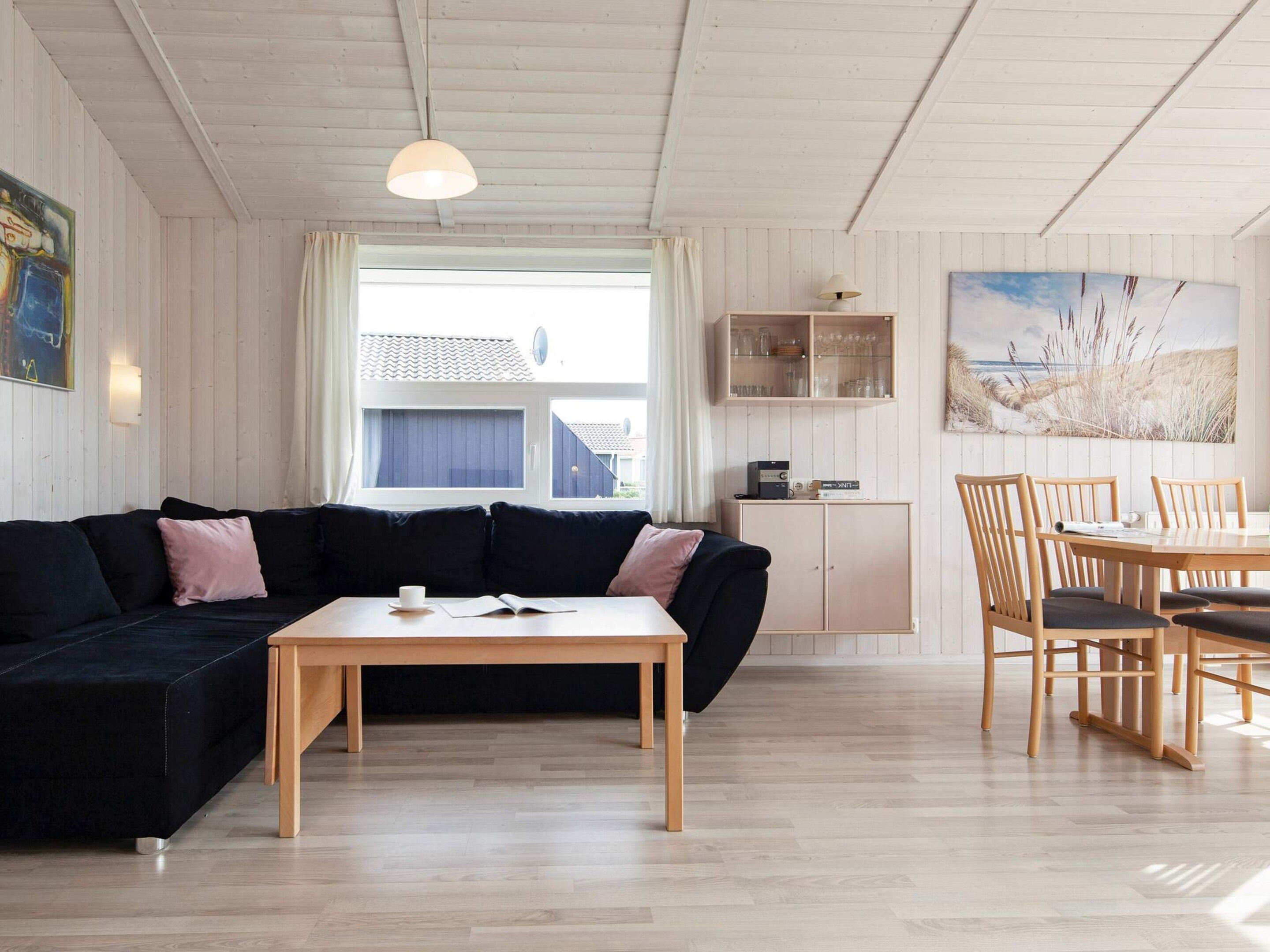 A modern living room with a black sofa, a wooden coffee table, and a dining area with wooden chairs and a table.